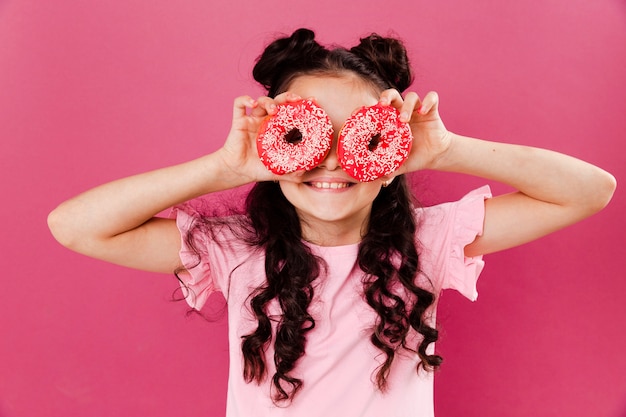 Kostenloses Foto kleines mädchen der vorderansicht, das mit doughntus spielt