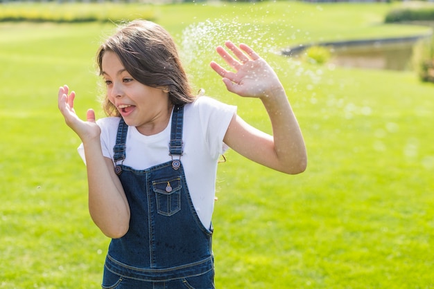 Kleines Mädchen der Vorderansicht, das mit einem Wasserwerfer gewässert wird