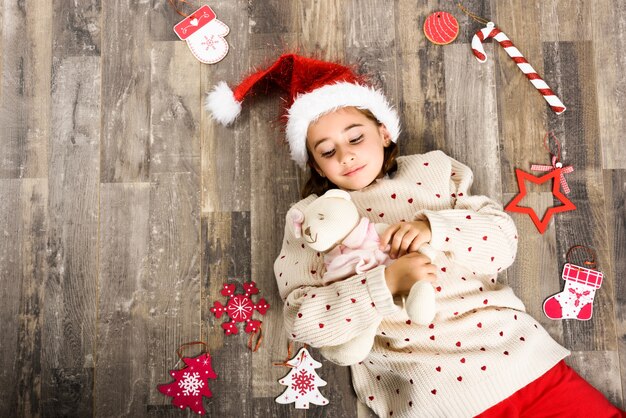 Kleines Mädchen gekleidet in Weihnachtsmann auf dem Rücken liegend umgeben von Weihnachten Dekorationen