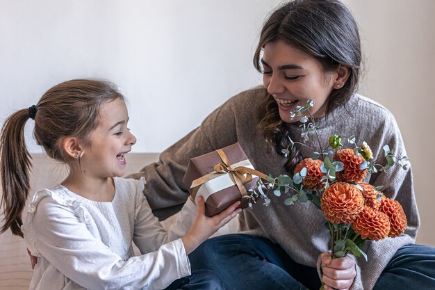 Kleines Mädchen gibt ihrer Mutter eine Geschenkbox und einen Strauß Chrysanthemenblumen, Konzept von Muttertag, Geburtstag, Frauentag.