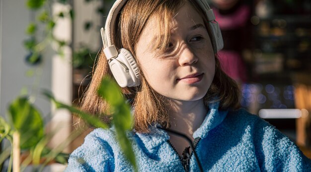 Kleines Mädchen hört Musik in Kopfhörern und trinkt Kakao mit sonnigem Morgen