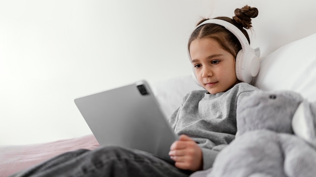 Kostenloses Foto kleines mädchen im bett mit kopfhörern mit tablette