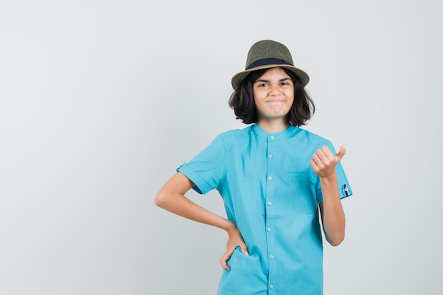 Kleines Mädchen im blauen T-Shirt, Hut zeigt Daumen hoch und sieht fröhlich aus