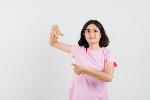 Kleines Mädchen im rosa T-Shirt, das Daumen oben und unten zeigt, Vorderansicht.