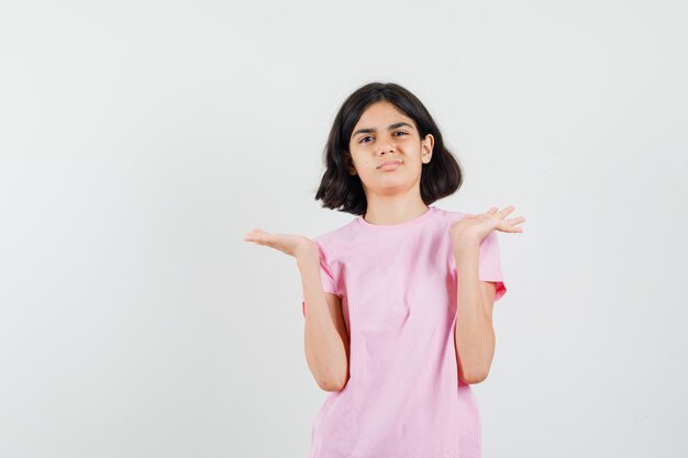 Kleines Mädchen im rosa T-Shirt gestikulieren wie etwas zeigen oder halten und Unzufriedenheit suchen, Vorderansicht.