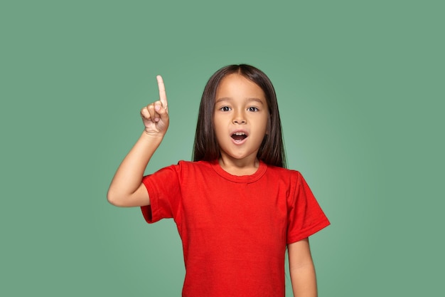 Kleines Mädchen im roten T-Shirt mit dem Finger nach oben auf grünem Hintergrund