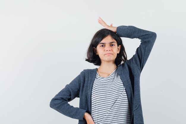 Kleines Mädchen im T-Shirt, Jacke, die Hand auf Kopf hält und zögernd aussieht