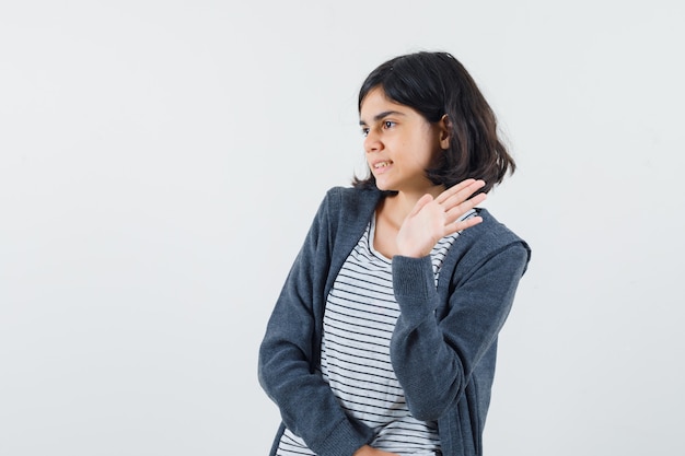 Kleines Mädchen im T-Shirt, Jacke, die Hand winkt, um sich zu verabschieden und fröhlich auszusehen