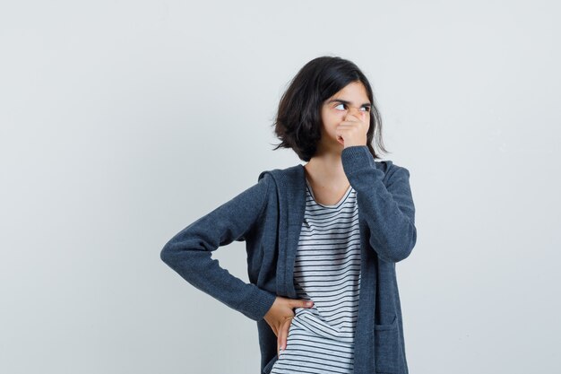 Kleines Mädchen im T-Shirt, Jacke, die ihre Nase hält und nachdenklich aussieht,