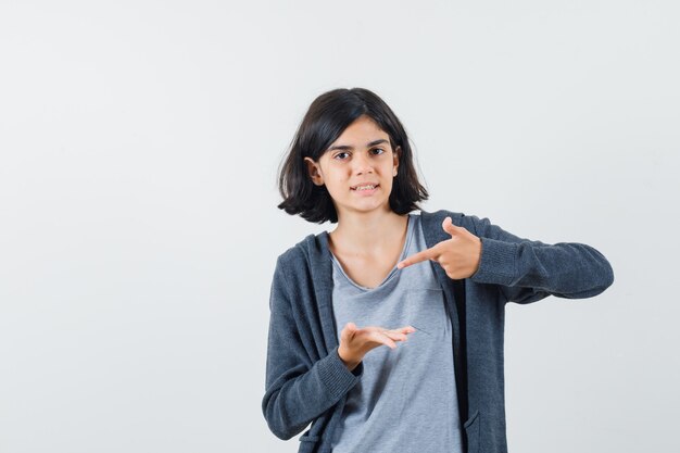 Kleines Mädchen im T-Shirt, Jacke zeigt auf ihre Handfläche und sieht selbstbewusst aus