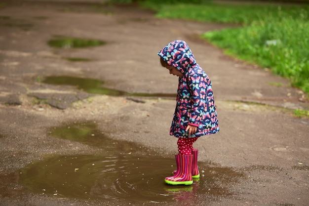Kleines Mädchen in den gumboots hat den Spaß, der in die Pools nach dem Regen geht
