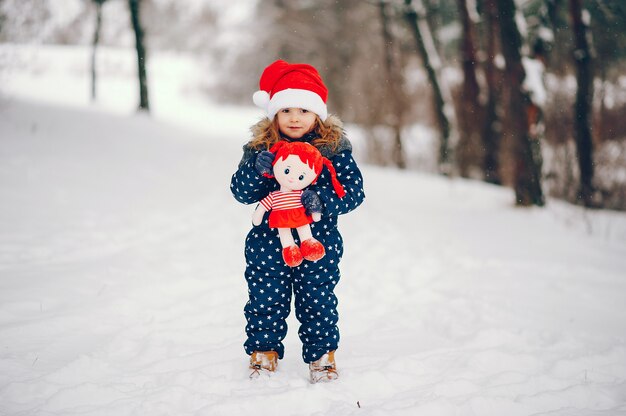 Kleines Mädchen in einem blauen Hut, der in einem Winterwald spielt