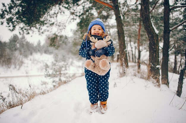 Kleines Mädchen in einem blauen Hut, der in einem Winterwald spielt