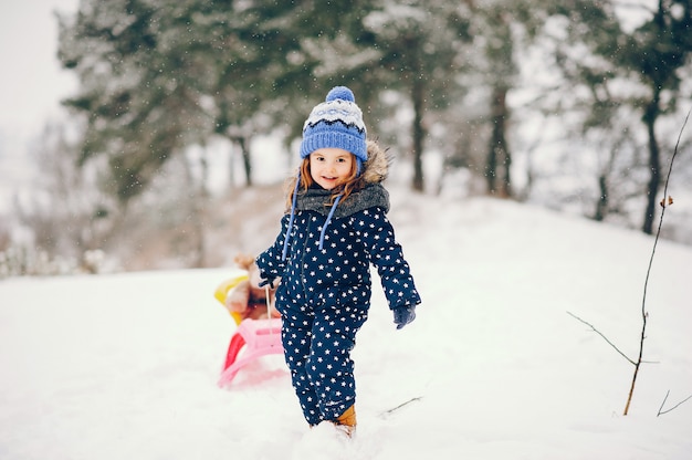 Kleines Mädchen in einem blauen Hut, der in einem Winterwald spielt