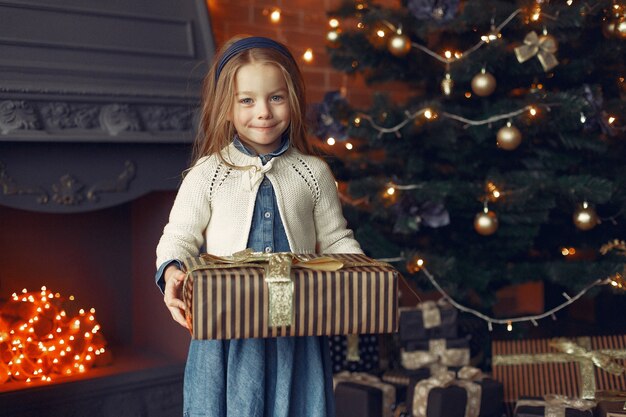 Kleines Mädchen in einem niedlichen Kleid nahe Weihnachtsbaum mit Geschenk