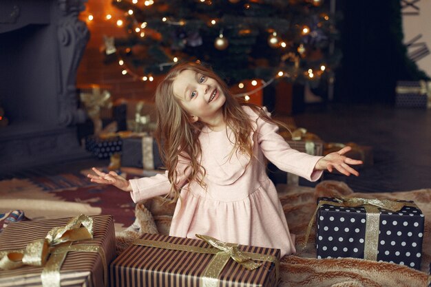 Kleines Mädchen in einem niedlichen Kleid nahe Weihnachtsbaum mit Geschenk
