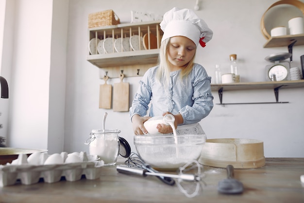 Kleines Mädchen in einem weißen Schafhut kochen den Teig für Plätzchen