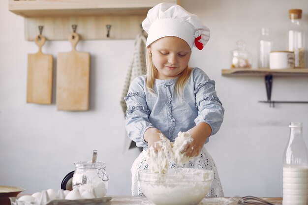 Kleines Mädchen in einem weißen Schafhut kochen den Teig für Plätzchen