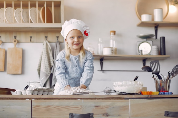 Kleines Mädchen in einem weißen Schafhut kochen den Teig für Plätzchen