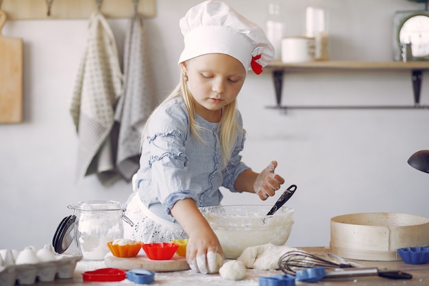 Kleines Mädchen in einem weißen Schafhut kochen den Teig für Plätzchen