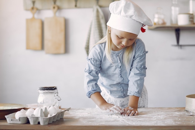 Kleines Mädchen in einem weißen Schafhut kochen den Teig für Plätzchen