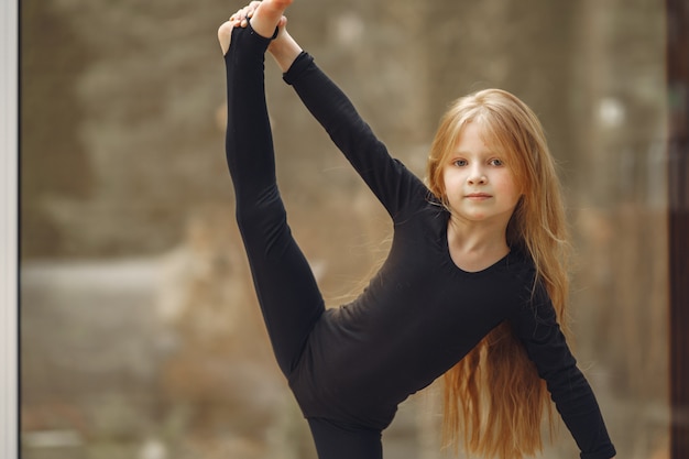 Kleines Mädchen in einer schwarzen Sportbekleidung ist mit Gymnastik beschäftigt