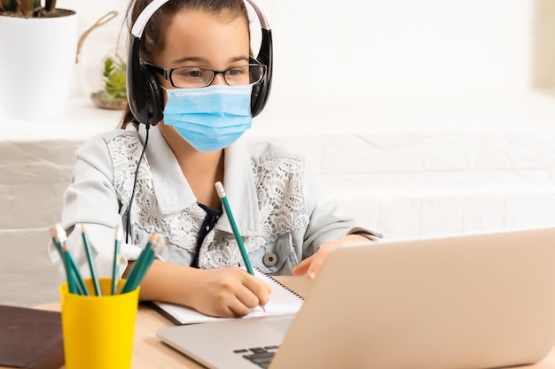 kleines Mädchen in medizinischer Maske, das zu Hause lernt. Epidemie Pandemie.