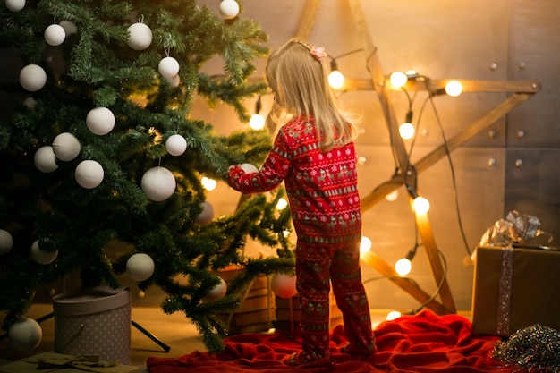 Kleines Mädchen in Pyjamas durch den Weihnachtsbaum