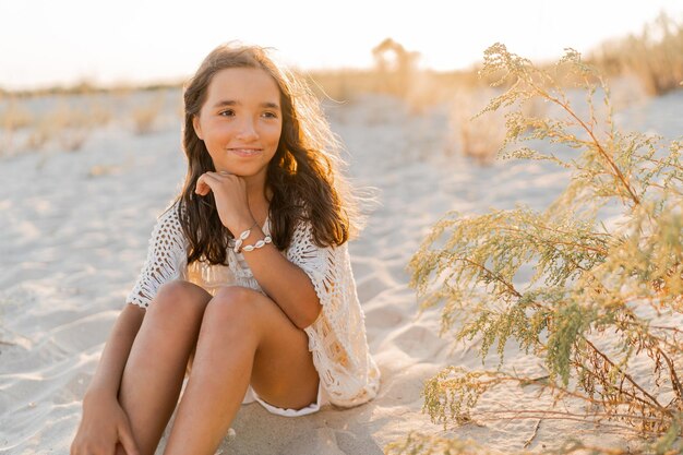 Kleines Mädchen in stylischem Boho-Sommeroutfit, das am Strand posiert Warme Sonnenuntergangsfarben Wach- und Reisekonzept