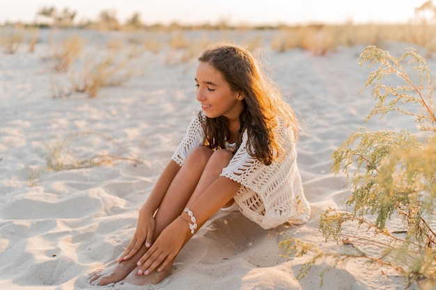 Kleines Mädchen in stylischem Boho-Sommeroutfit, das am Strand posiert Warme Sonnenuntergangsfarben Wach- und Reisekonzept