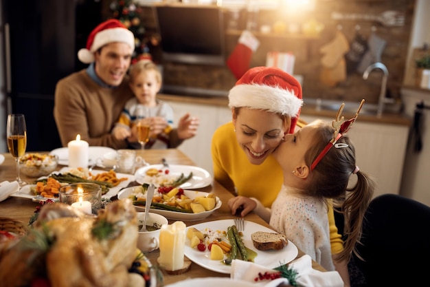 Kleines Mädchen küsst ihre Mutter beim Familienessen am Weihnachtstag