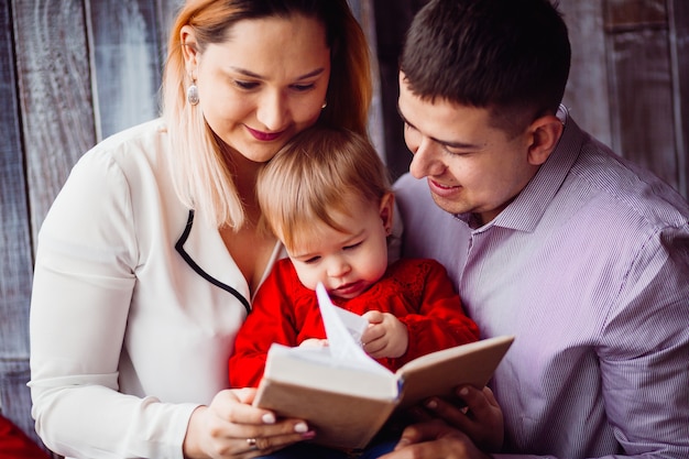 Kleines Mädchen liest ein Buch, das mit Mutter und Vati sitzt