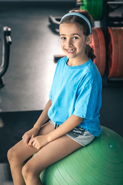 Kleines Mädchen macht Übungen mit einem großen Ball im Fitnessstudio