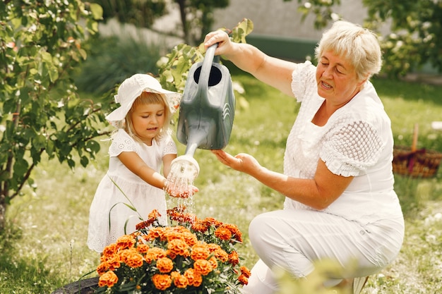 Kleines Mädchen mit älterer Großmutter, die im Hinterhofgarten arbeitet. Kind in einem weißen Hut.