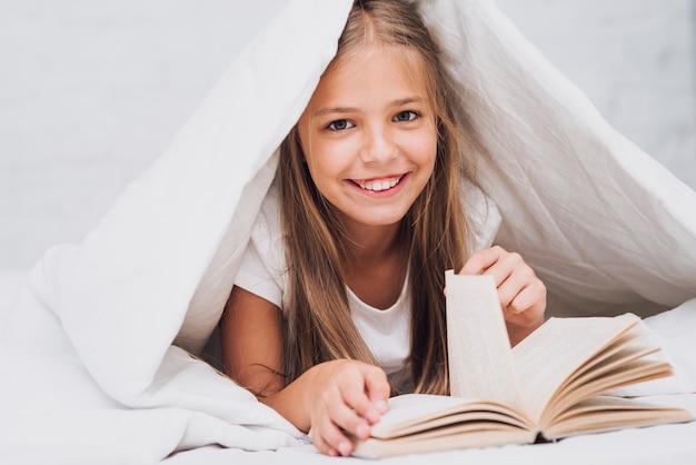 Kostenloses Foto kleines mädchen mit dem buch, welches die kamera betrachtet