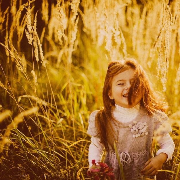 Kleines Mädchen mit dem roten Haar steht auf dem Herbstfeld
