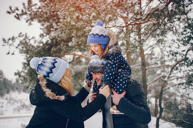 Kleines Mädchen mit den Eltern, die in einem Winterpark spielen