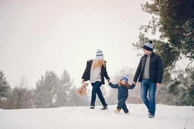 Kleines Mädchen mit den Eltern, die in einem Winterpark spielen