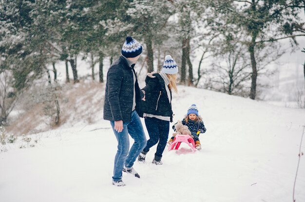 Kleines Mädchen mit den Eltern, die in einem Winterpark spielen