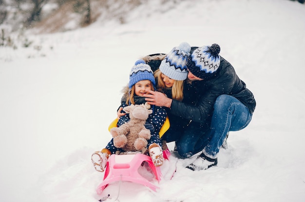 Kleines Mädchen mit den Eltern, die in einem Winterpark spielen