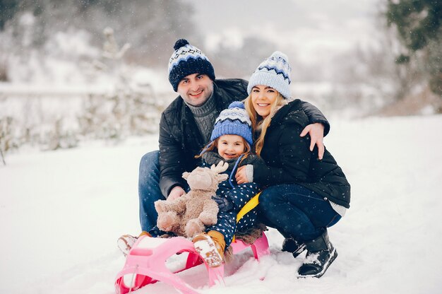 Kleines Mädchen mit den Eltern, die in einem Winterpark spielen