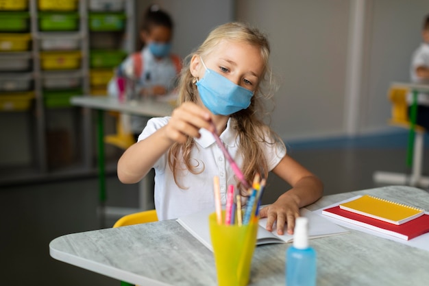 Kostenloses Foto kleines mädchen mit der medizinischen maske, die einen bleistift nimmt