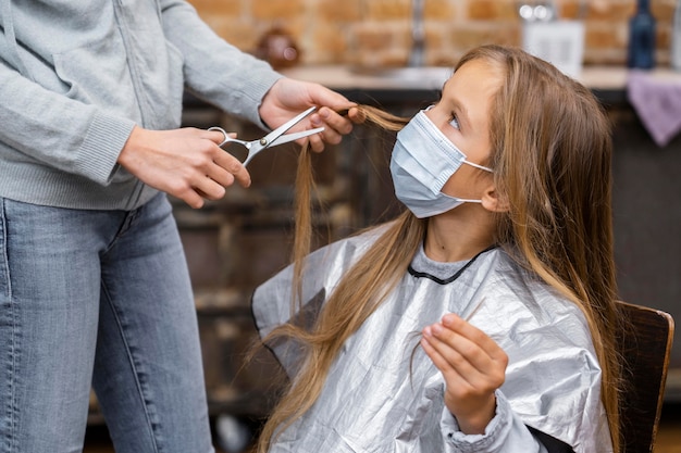 Kostenloses Foto kleines mädchen mit der medizinischen maske, die einen haarschnitt bekommt