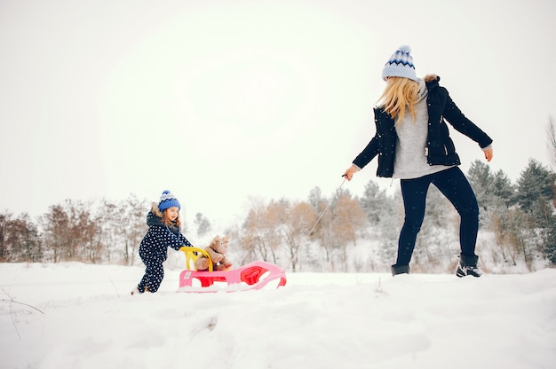 Kleines Mädchen mit der Mutter, die in einem Winterpark spielt