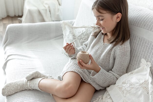 Kleines Mädchen mit einem Fadenknäuel und einer Nadel zu Hause auf der Couch.