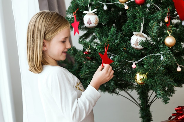 Kleines Mädchen mit einem roten Stern der Weihnachtsbaum spielen