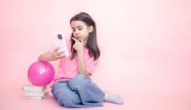 Kleines Mädchen mit einem Smartphone in ihren Händen auf einem rosa Hintergrundkopierraum