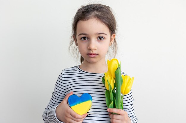 Kleines Mädchen mit einem Strauß Tulpen und einem Herzen mit der Flagge der Ukraine