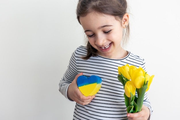 Kleines Mädchen mit einem Strauß Tulpen und einem Herzen mit der Flagge der Ukraine