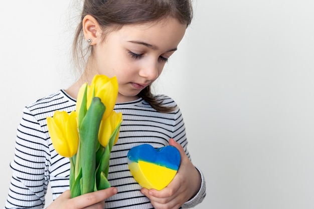 Kleines Mädchen mit einem Strauß Tulpen und einem Herzen mit der Flagge der Ukraine